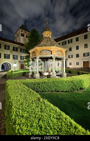 Novacella Abbey: Der „Wunderbrunnen“ im Innenhof und der Glockenturm mit der Uhr. Varna, Südtirol, Italien. Stockfoto