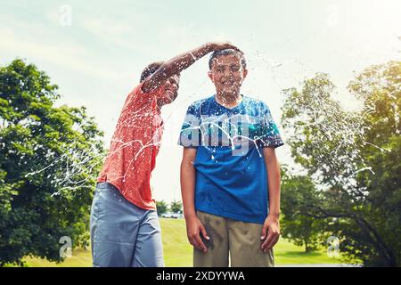 Wasserballons, Planschen und Jungen im Park mit Freiheit, Spaß oder Verbundenheit mit nassen, Sommer- oder Urlaubsspielen in der Natur. Glücklich, Energie und Freunde sind da Stockfoto