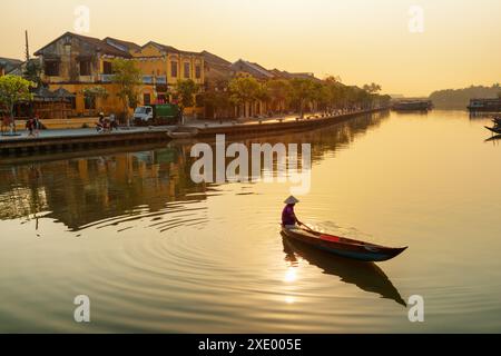 Herrlicher Blick auf die vietnamesische Frau in traditionellem Bambushut auf einem Holzboot auf dem Fluss Thu Bon in der antiken Stadt Hoi an bei Sonnenaufgang in Vietnam. Stockfoto