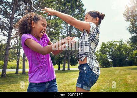 Wasserballons, Lachen und Mädchen im Park mit Freiheit, Spaß und Verbundenheit beim Lernen in der Natur. Fröhlich, plansch und kindlich befreundet mit flüssigem Kampf Stockfoto