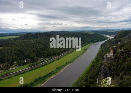 Ein Fluss mit einem Zug, der vorbeifährt. Der Zug fährt viele Autos. Der Himmel ist bewölkt Stockfoto