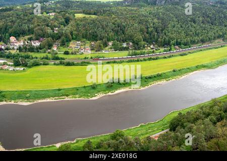 Ein Zug fährt einen Fluss in der Nähe einer Stadt hinunter. Der Zug ist rot und der einzige auf den Gleisen Stockfoto