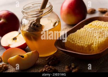 Einmachglas mit Honig, Honigtaube, Honigwabe, roten Äpfeln und Walnüssen auf Küchentisch Stockfoto