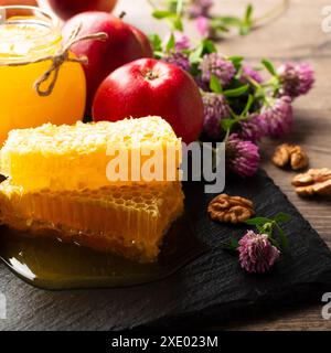 Einmachglas mit Honig, Honigwabe, roten Äpfeln und Walnüssen auf Küchentisch Stockfoto