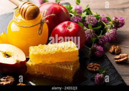 Einmachglas mit Honig, Honigtaube, Honigwabe, roten Äpfeln und Walnüssen auf Küchentisch Stockfoto