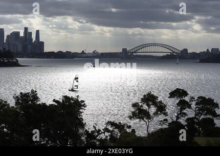 Ein einzelnes Segelboot auf einem silbernen Hafen von Sydney in Rose Bay am Nachmittag, die Skyline von Sydney, die Harbour Bridge und das Opernhaus im Hintergrund Stockfoto