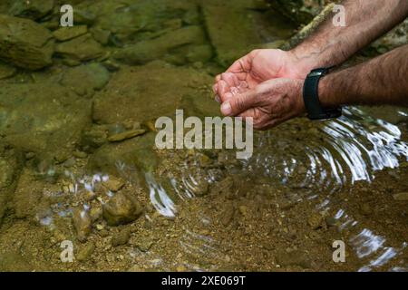 Die Hände des Mannes nehmen Wasser aus einem Fluss aus kristallklarem Wasser Stockfoto