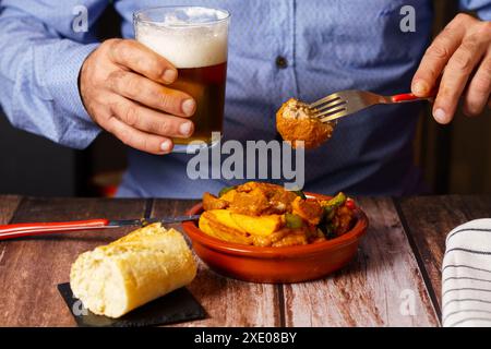 Mann mit Bart isst Fleischbällchen mit Spaghetti mit einem Glas Bier in der Hand Stockfoto