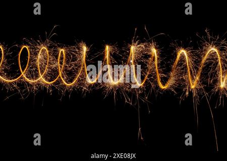Spiralförmige Leuchten mit Funken auf schwarzem Hintergrund. Weihnachtsbeleuchtung bei langer Belichtung. Stockfoto