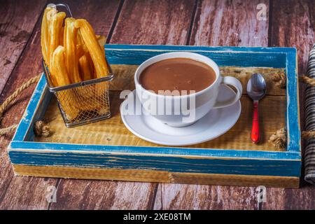 Heiße Schokolade in einem weißen Becher mit Churros in einem blauen Holztablett Stockfoto