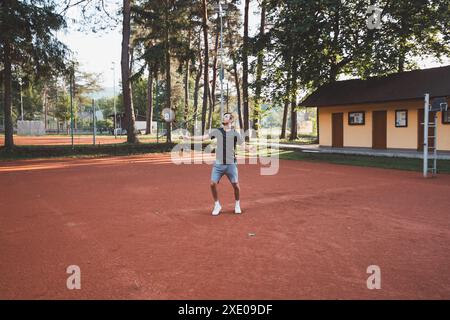 Ein schwarzhaariger Athlet mit einem Lächeln im Gesicht spielt Badminton auf einem Tonplatz. Begeisterung für den Amateursport. Lernen neuer Bewegungsfähigkeiten. Stockfoto