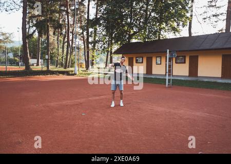 Ein schwarzhaariger Athlet mit einem Lächeln im Gesicht spielt Badminton auf einem Tonplatz. Begeisterung für den Amateursport. Lernen neuer Bewegungsfähigkeiten. Stockfoto