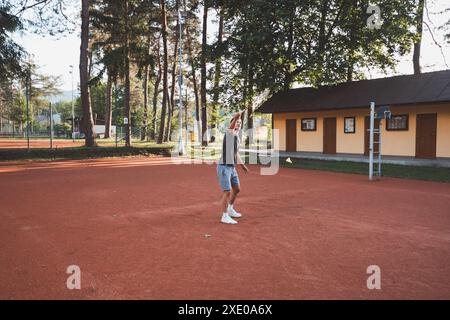 Ein schwarzhaariger Athlet mit einem Lächeln im Gesicht spielt Badminton auf einem Tonplatz. Begeisterung für den Amateursport. Lernen neuer Bewegungsfähigkeiten. Stockfoto