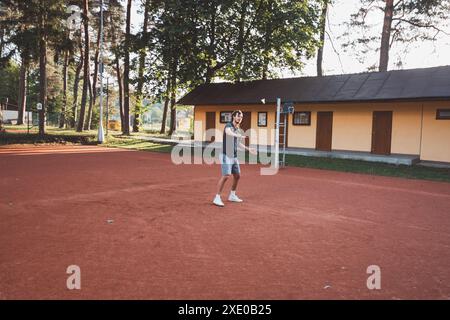 Ein schwarzhaariger Athlet mit einem Lächeln im Gesicht spielt Badminton auf einem Tonplatz. Begeisterung für den Amateursport. Lernen neuer Bewegungsfähigkeiten. Stockfoto