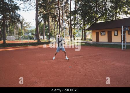 Ein schwarzhaariger Athlet mit einem Lächeln im Gesicht spielt Badminton auf einem Tonplatz. Begeisterung für den Amateursport. Lernen neuer Bewegungsfähigkeiten. Stockfoto