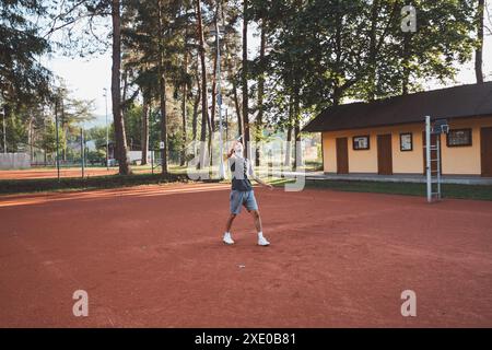 Ein schwarzhaariger Athlet mit einem Lächeln im Gesicht spielt Badminton auf einem Tonplatz. Begeisterung für den Amateursport. Lernen neuer Bewegungsfähigkeiten. Stockfoto