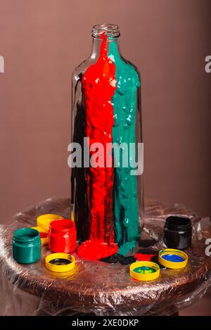 Geschlossenes Porträt einer Glasflasche mit Töpfen mit Farben in weiß, schwarz, gelb, grün, blau und rot. Abstrakt. Isoliert auf braunem Hintergrund. Stockfoto