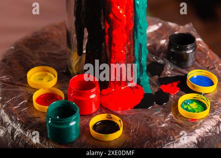 Geschlossenes Porträt einer Glasflasche mit Töpfen mit Farben in weiß, schwarz, gelb, grün, blau und rot. Abstrakt. Isoliert auf braunem Hintergrund. Stockfoto