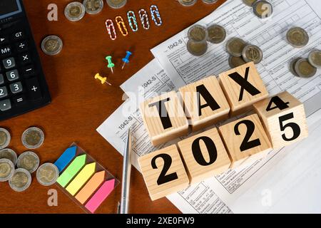 Ein Holzblock mit dem Wort "Steuer" drauf steht auf einem Stapel Münzen und einem Rechner. 2024 Gehen Sie zu 2025. Zahlung des Steuersatzes. Steuern, Steuerlast. Bus Stockfoto
