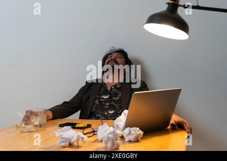 Asiatischer Geschäftsmann versagt, Mann in Verzweiflung trinkt harten Alkohol, sitzt spät am Tisch im Büro, depressiv und hoffnungslos. Das Konzept des Alkoholismus bei Stockfoto