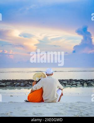 Liebe Paare, die gemeinsam den Sonnenaufgang in den Sommerferien am Strand beobachten. Die Silhouette der Leute von hinten sitzend genießt den Blick auf die tropische Insel des Meeres Stockfoto