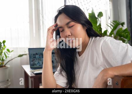 Frustrierte junge Frau, die am Schreibtisch vor dem Laptop arbeitet und an täglichen chronischen Kopfschmerzen leidet, Online-Behandlung, Termin, ärztliche Beratung, Stockfoto