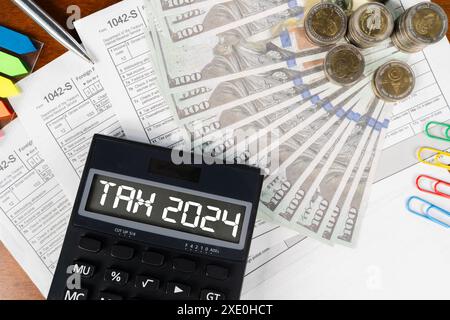 Ein Taschenrechner mit dem Wort "Steuer 2024" ist auf einem Haufen Geld. Der Rechner ist schwarz und das Geld ist in verschiedenen Stückelungen. Stockfoto