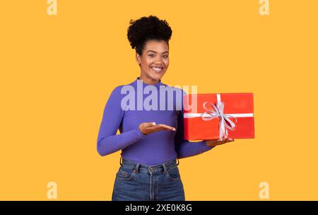 Lächelnde Frau, Die Rote Geschenkbox Vor Gelbem Hintergrund Hält Stockfoto