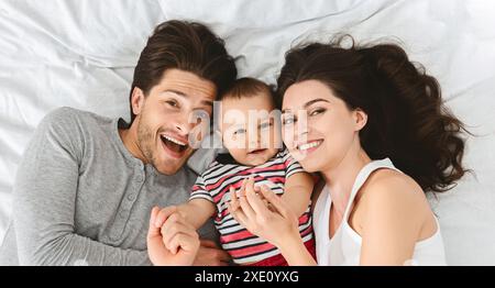 Glückliche Dreierfamilie, die auf weißem Bett liegt Stockfoto