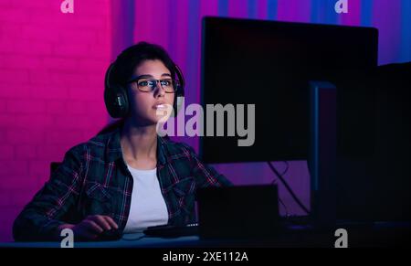 Junge Frau, die Brillen und Kopfhörer trägt, benutzt den Computer Stockfoto