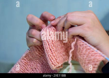 Stricken mit Stricknadeln. Der Anblick einer Frauenhand, die einen rosa Schal strickt. Nahaufnahme Stockfoto