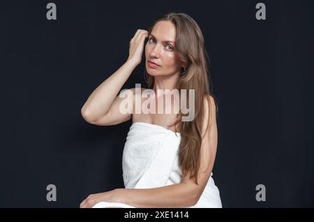 Porträt einer attraktiven Frau mit langen Haaren in weißem Handtuch auf schwarzem Hintergrund Stockfoto
