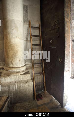 Die Leiter lehnt sich an die Mauer nahe der Tür zum Eingang der Grabeskirche, und der muslimische Mann namens Nusseibeh klettert sie, um das Tor zu öffnen Stockfoto