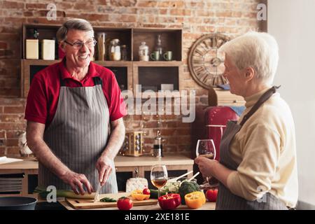 Senior-Paar Kocht Zusammen In Der Küche Mit Brick Wall, Plaudert Stockfoto