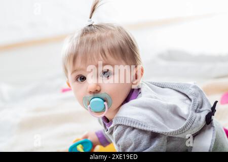 Glückliches Mädchen kriecht auf einer Decke, umgeben von Spielzeug, strahlt Unschuld und Freude aus. Ihr Ausdruck zeigt Staunen und Neugier und symbolisiert Familien Stockfoto