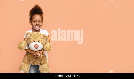 Happy Black Little Girl Hält Teddybär Vor Peach Hintergrund Stockfoto