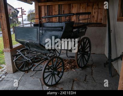 Eine altmodische Pferdekutsche, die unter einem Holzunterstand in einer rustikalen Umgebung im Freien parkt. Stockfoto