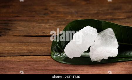 Ein Korb, gefüllt mit weißen Alaun-Kristallen, sitzt auf einem leuchtend grünen Strauchhintergrund. Die Kontrastfarben heben die Reinheit des Alaums gegenüber dem hervor Stockfoto