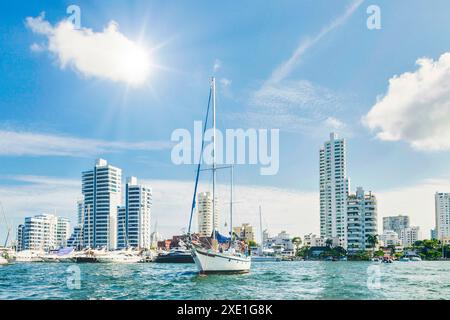 Segelboote vor dem Hintergrund moderner Hochhäuser und eines hellblauen Himmels mit flauschigen Wolken vor einem ruhigen Hafen der Küstenstadt ankern. Stockfoto