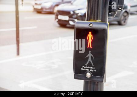 Nahaufnahme eines Fußgängersignals mit dem roten Wartsymbol, das entlang einer belebten Straße im Stadtzentrum leuchtet Stockfoto