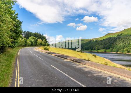 Einsame, kurvenreiche Straße, die an einem klaren Sommertag entlang eines Stausees in den Bergen verläuft Stockfoto