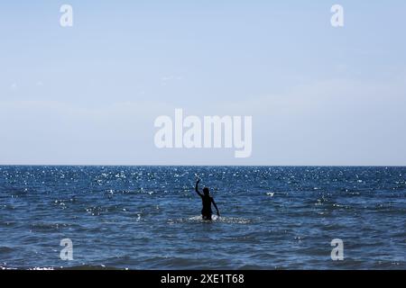 Ein beruhigendes Bild, das eine Einzelfigur zeigt, die im glitzernden Meer steht und ein Gefühl von Frieden und Einsamkeit vermittelt. Stockfoto