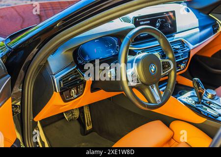 Innenansicht des neuen BMW i4 M Elektroautos aus Fahrerperspektive mit Lenkrad, Navigationsleiste und orangefarbener Lederpolsterung. Stockfoto