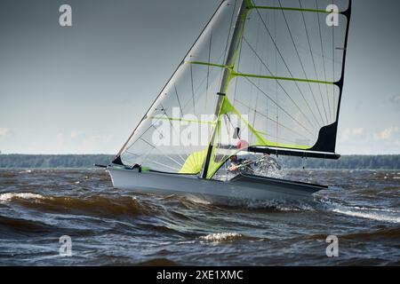 Der Blick auf das Sportsegelboot ist bei Sonnenuntergang hoch, Sportler neigen das Boot, Geschwindigkeit und Spritzwasser, Reflexion der Sonne auf der Wasseroberfläche Stockfoto