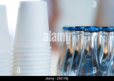 Nahaufnahme von gestapelten weißen Pappbechern und Glasflaschen mit blauen Kappen. Stockfoto