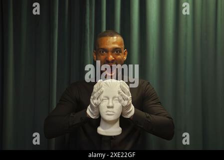 Afroamerikaner hält und drückt den Kopf der Schaufensterpuppe. Der Typ schreit. Hintergrund grün, Vorhang. Stockfoto