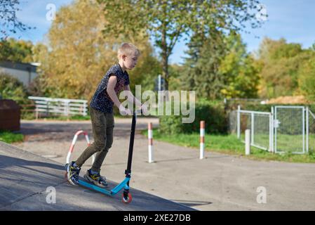 Kind auf einem Tretroller im Park. Kinder lernen Rollbrett laufen. Kleiner Junge, der an sonnigen Sommertagen Schlittschuhlaufen kann. Outdoor-Aktivitäten für ch Stockfoto