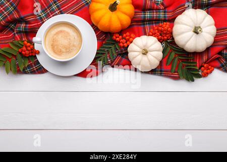 Eine Tasse Kaffee auf einer karierten Decke mit Herbstblättern und Kürbissen kopieren den weißen Holzhintergrund Stockfoto