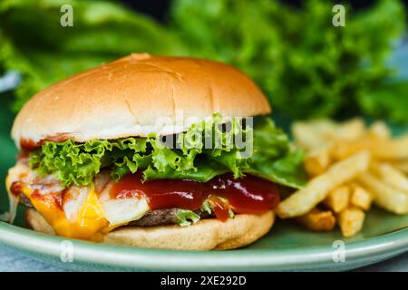 Nahaufnahme des hausgemachten amerikanischen Cheeseburgers, französisches gebratenes und grünes Gemüse. Stockfoto