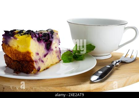 Nahaufnahme eines Joghurtstücks mit Heidelbeerkuchen in einer weißen Keramikschale mit einer Tasse Kaffee und einer Metallgabel. Stockfoto